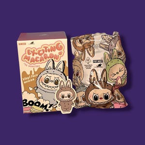K&ouml;nnte beinhalten: Eine Pop Mart-Box und ein versiegelter Beutel mit The Monsters "Exciting Macaron" Vinyl-Gesichtsfiguren. Die Box ist beige mit rosa Text und einem Cartoon-Hasen-Design. Der Beutel zeigt verschiedene hasenartige Charaktere.
