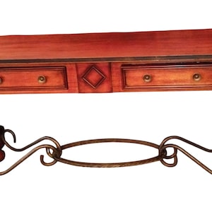 May include: A rectangular wooden console table with a reddish-brown finish, featuring two drawers with small round knobs, a central diamond-shaped accent, four turned legs, and a decorative dark metal scrollwork stretcher connecting the base.