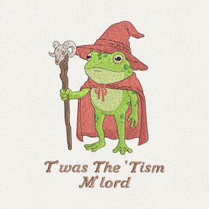 May include: An embroidered design featuring a green frog dressed as a wizard, wearing a red hat and cape, and holding a staff with a ram's skull. The text "T'was The 'Tism M'lord" is below the frog.