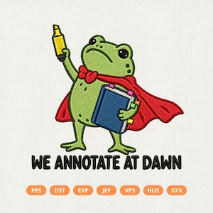 May include: An embroidery design featuring a green frog wearing a red cape, holding a yellow highlighter and a blue book. Below the frog, the text reads "WE ANNOTATE AT DAWN" in black, followed by a row of file format labels: PES, DST, EXP, JEF, VP3, HUS, XXX.