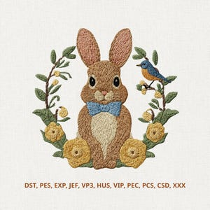 May include: Embroidered design featuring a brown bunny wearing a blue bow tie, surrounded by a floral wreath with yellow flowers and a blue bird. The design is on a white background. The image includes text at the bottom.