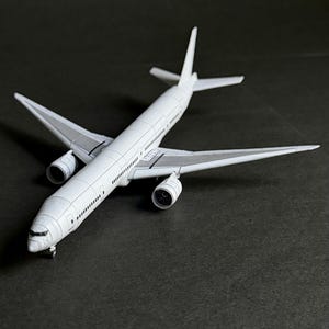 May include: A white scale model aeroplane featuring two jet engines mounted under the wings, a long fuselage with visible window markings, a vertical stabiliser, and horizontal tail wings, captured from a high-angle perspective.