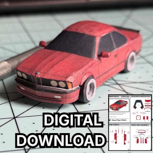 Puede incluir: Un modelo de papel rojo de un coche BMW 635CSi a escala 1/64, con ruedas blancas. El modelo tiene ventanas negras y un frontal detallado. El texto "DIGITAL DOWNLOAD" se muestra debajo. Se incluyen diagramas.