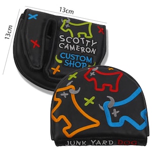 May include: Black golf club head cover, 13cm x 13cm, with colorful embroidered bull graphics and the text "SCOTTY CAMERON CUSTOM SHOP" and "JUNK YARD DOG". The cover has a magnetic closure.