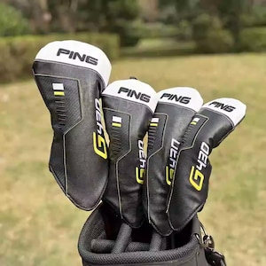 Puede incluir: Un conjunto de fundas para palos de golf en blanco y negro con la marca "PING" impresa. Las fundas tienen detalles amarillos y el texto "G430". Las fundas para palos de golf están en una bolsa de golf negra.
