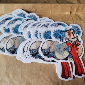 May include: A stack of stickers featuring a blue-haired creature with a red scarf. The creature has a white face with red markings and a surprised expression.