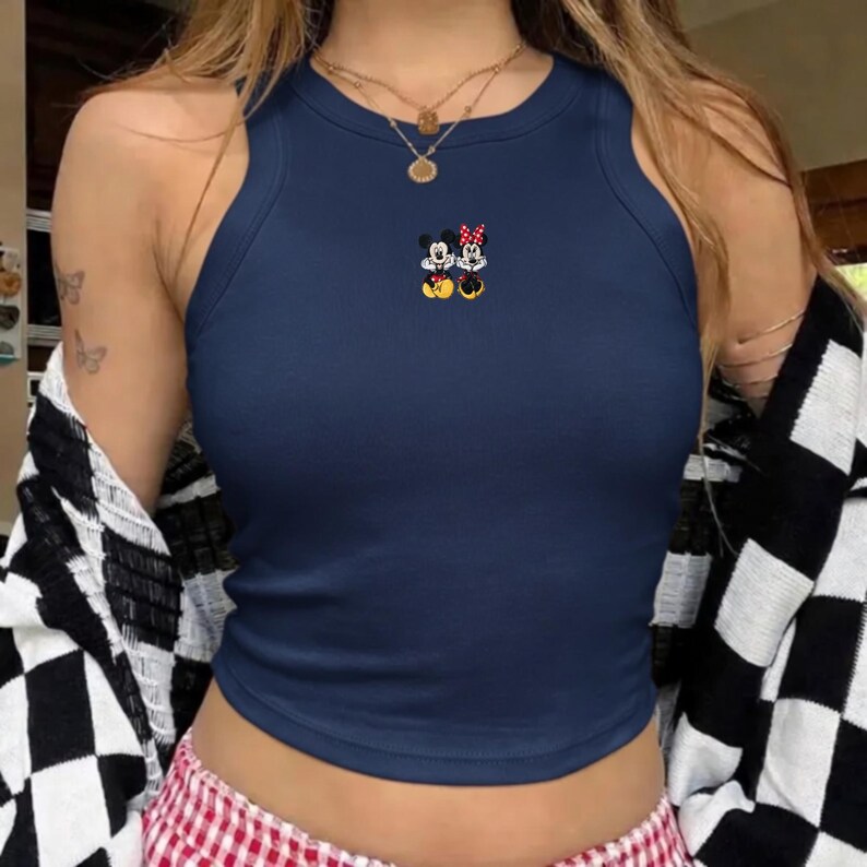 Puede incluir: Camiseta sin mangas de canal&eacute; azul marino con un bordado de Mickey y Minnie Mouse. La camiseta sin mangas tiene un cuello redondo y se lleva con una chaqueta a cuadros blancos y negros y unos pantalones cortos a cuadros rojos y blancos. La camiseta es de estilo corto.