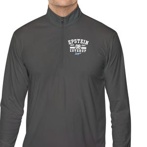 Könnte beinhalten: Ein dunkelgrauer Langarm-Pullover mit kurzem Reißverschluss am Kragen und einer weißen Grafik auf der linken Brust, die den Schriftzug EPSTEIN EST 08 COVERUP in einem universitären Schriftstil zeigt. Das Kleidungsstück hat einen Stehkragen.