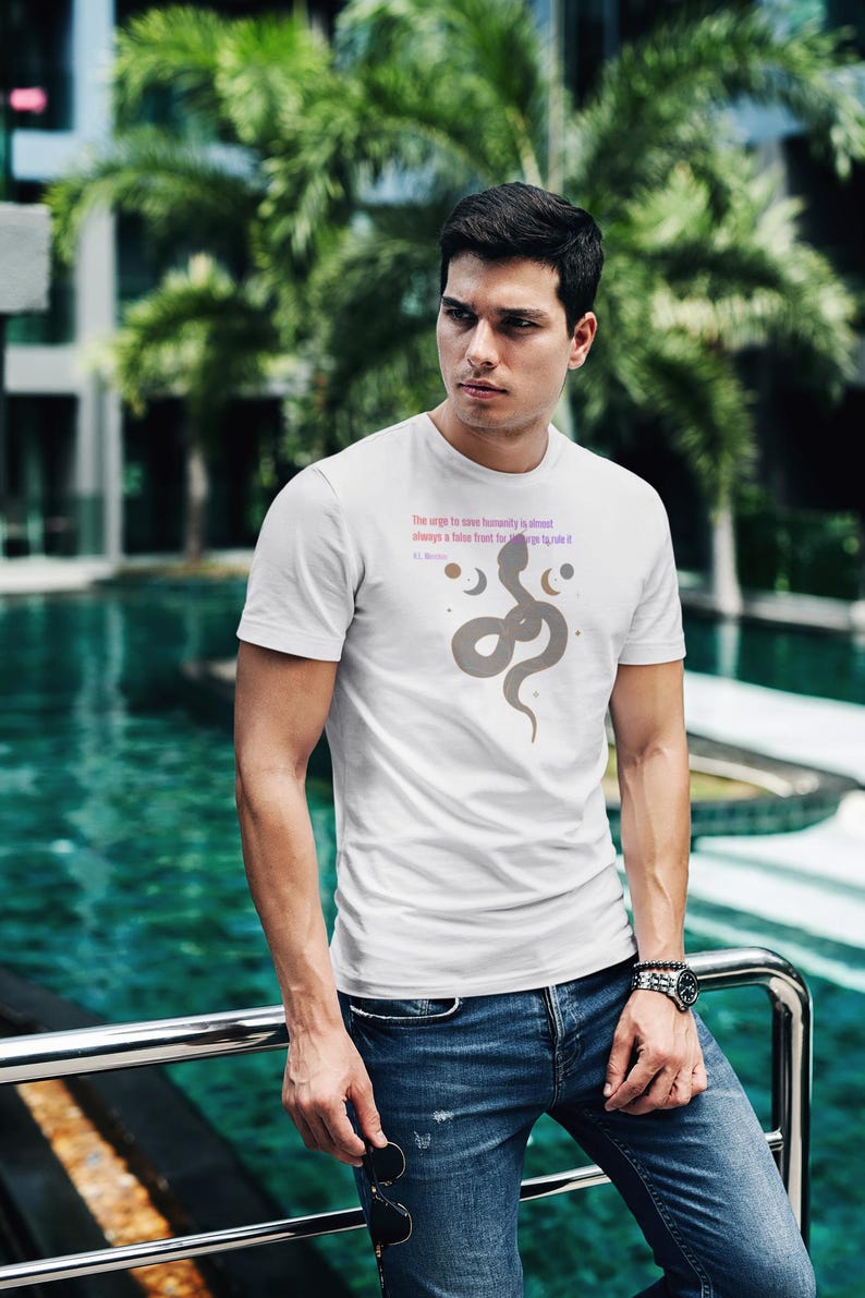 May include: White t-shirt with a gray snake graphic and text. The shirt features a crew neck and short sleeves. The text reads "The urge to save humanity is almost always a false front for the urge to rule it".