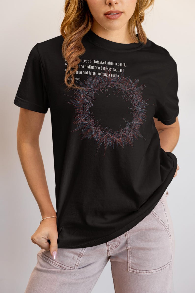 May include: A black short-sleeve t-shirt featuring a circular abstract graphic in red and blue lines. The text reads: The ideal subject of totalitarianism is people for whom the distinction between fact and fiction, true and false, no longer exists. Hannah Arendt.
