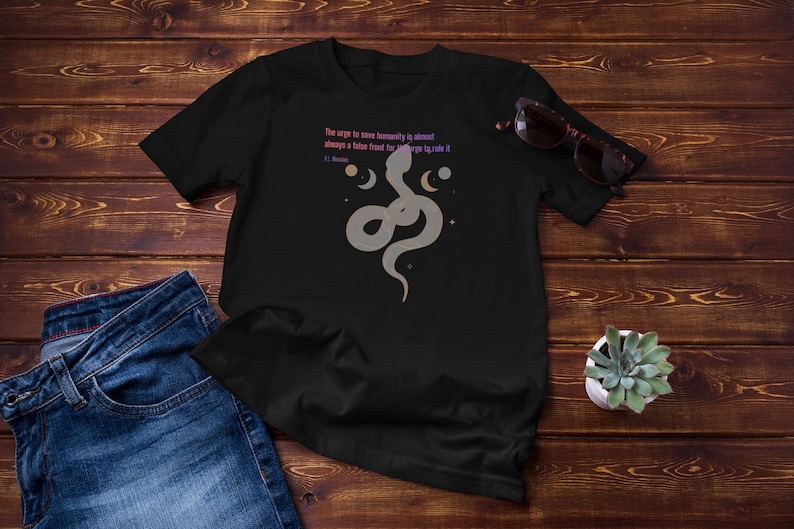 May include: Black t-shirt with a gray snake graphic, moons, and stars. The shirt features the quote "The urge to save humanity is almost always a false front for the urge to rule it." Sunglasses and a small succulent are also visible.