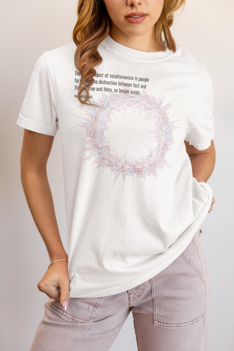 May include: A white short-sleeved t-shirt featuring a circular graphic composed of red and blue lines. Above the graphic, black text reads: The ideal subject of totalitarianism is people for whom the distinction between fact and fiction, true and false, no longer exists. Hannah Arendt.
