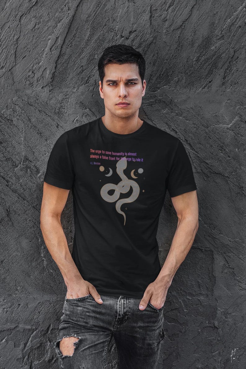 May include: Black t-shirt featuring a stylized gray snake design with text that reads "The urge to save humanity is almost always a false front for the urge to rule it." The design includes crescent moons and stars.