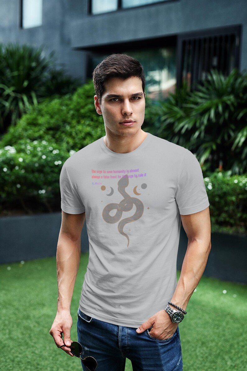 May include: A light gray t-shirt featuring a stylized snake design with text. The text reads "The urge to save humanity is almost always a false front for the urge to rule it." The shirt is worn by a person.