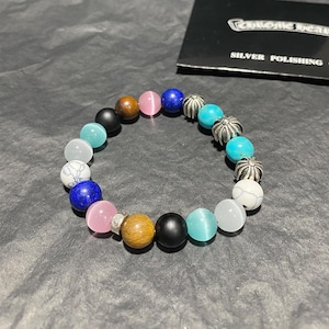 Puede incluir: Una pulsera de cuentas multicolores con una variedad de cuentas redondas. La pulsera incluye cuentas en tonos rosa, azul, turquesa, marrón, negro y blanco, con algunos detalles plateados. Las cuentas están ensartadas para formar un círculo completo.