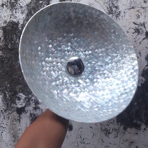 May include: A decorative, iridescent bowl with a mosaic-like pattern. The bowl has a silver-colored, circular base in the center. The bowl is held by a person.