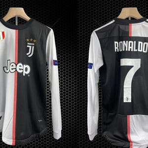 May include: A long-sleeved soccer jersey, split vertically with black and white panels. The front features the Jeep logo, team emblem, and a red stripe. The back displays "RONALDO" and the number 7. The jersey hangs on a wooden hanger.
