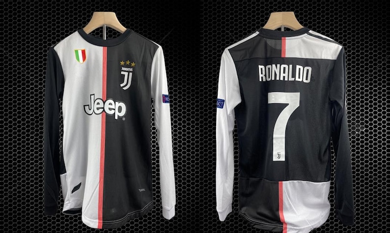 May include: A long-sleeved soccer jersey, split vertically with black and white panels. The front features the Jeep logo, team emblem, and a red stripe. The back displays "RONALDO" and the number 7. The jersey hangs on a wooden hanger.