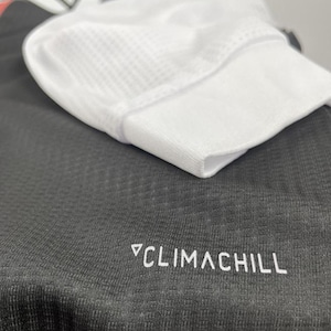 May include: Close-up of a white athletic cap with a mesh top, resting on a dark gray athletic shirt. The shirt has the text "CLIMACHILL" printed in white.
