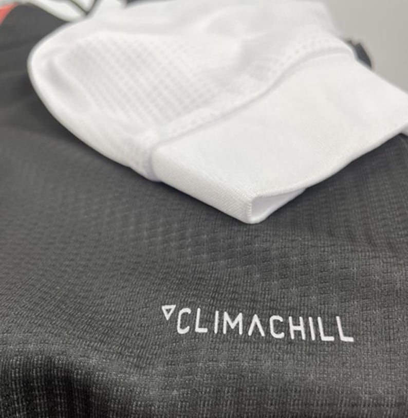 May include: Close-up of a white athletic cap with a mesh top, resting on a dark gray athletic shirt. The shirt has the text "CLIMACHILL" printed in white.