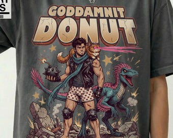 May include: A charcoal gray t-shirt featuring a graphic print with the text "GODDAMNIT DONUT". The illustration depicts a person in a leather vest and heart-patterned boxers holding a bomb, accompanied by a cat and a blue dinosaur. The shirt has a Comfort Colors label.