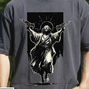 May include: Dark gray t-shirt featuring a black and white graphic of a figure with a halo holding two guns. The figure is depicted in flowing robes. The shirt has the word "PEPPER" in a white box at the bottom.