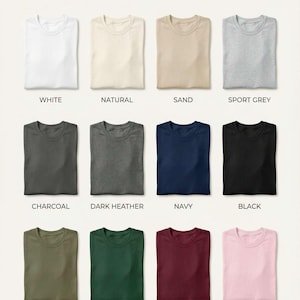 May include: A Gildan 5000 classic color palette chart displaying twelve folded t-shirts in white, natural, sand, sport grey, charcoal, dark heather, navy, black, military green, forest green, maroon, and light pink with corresponding labels.