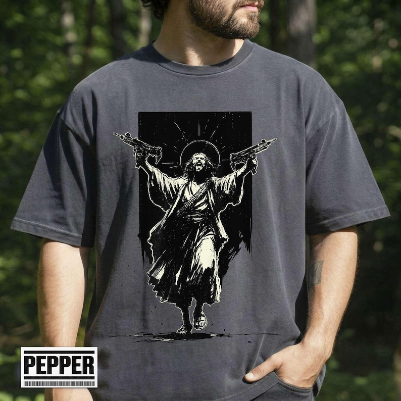 May include: Dark gray t-shirt featuring a black and white graphic of a figure with a halo holding two guns. The figure is depicted in flowing robes. The shirt has the word "PEPPER" in a white box at the bottom.