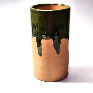 May include: A cylindrical terracotta vase featuring a smooth, unglazed light brown lower section and a glossy, dark forest green glazed upper rim. The green glaze drips down the sides in irregular, vertical patterns over the natural clay.