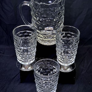 May include: A clear glass pitcher and three matching tall glasses, all featuring a textured, geometric honeycomb pattern. The pitcher has a curved handle and a scalloped rim, while each glass stands on a circular base, creating a cohesive set.