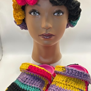 May include: A colorful crochet hat and matching clogs. The hat features a wavy brim in pink, yellow, and black. The clogs are pink with crochet in black, yellow, purple, and teal. The items are displayed on a mannequin head.