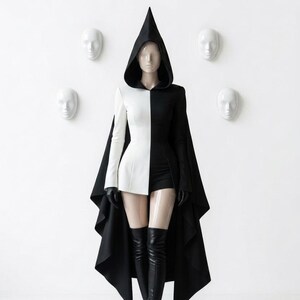 May include: A two-toned black and white hooded jacket with a long, flowing cape back, paired with black shorts, black gloves, and black over-the-knee boots. The garment features a sharp, pointed hood and a split color design that divides the piece vertically.
