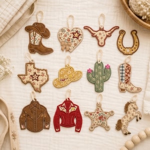 Può includere: Una collezione di dodici ornamenti da appendere ricamati con forme a tema western, tra cui uno stivale da cowboy, un cuore, un teschio di longhorn, un ferro di cavallo, la mappa del Texas, un cappello, un cactus, una camicia, una giacca, una stella e un cavallo.