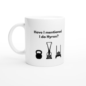May include: White ceramic mug with the text "Have I mentioned I do Hyrox?" and black illustrations of a kettlebell, a ski erg, and a weight sled. The mug has a curved handle.