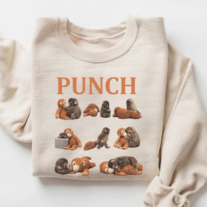 May include: Beige crewneck sweatshirt with the word "PUNCH" in orange block letters. The sweatshirt features a repeating pattern of cartoon monkeys in various poses, in shades of brown and gray.