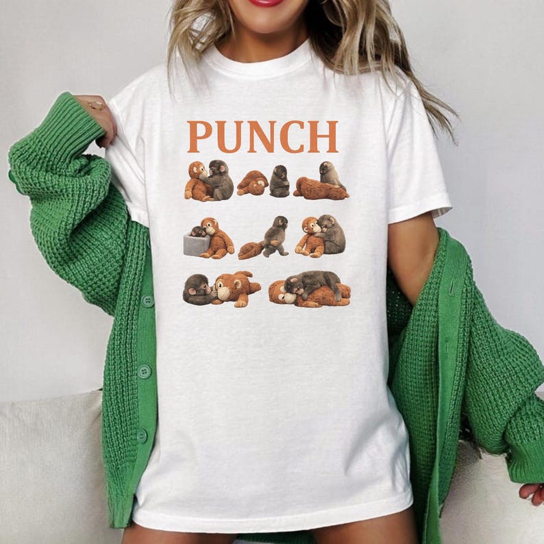 May include: White t-shirt with the word "PUNCH" in orange letters. The shirt features a graphic of several small, plush monkey toys in various poses. The monkeys are brown and gray.