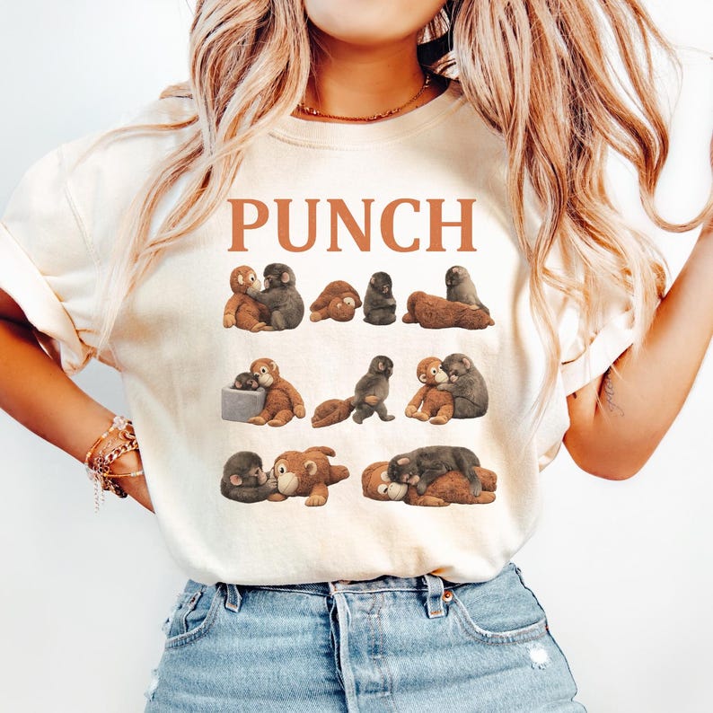 May include: Cream-colored t-shirt with the word "PUNCH" in brown block letters. The shirt features a repeating pattern of cartoon monkeys in various poses, in shades of brown and gray.
