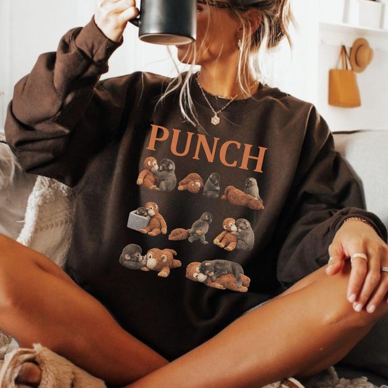 May include: A brown sweatshirt with the word "PUNCH" in orange block letters. The sweatshirt features a pattern of small, plush animal figures in various poses. The person is holding a black mug.