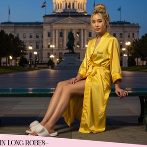 May include: A yellow satin robe with the word "Bride" embroidered on the front. The robe has a matching belt and is knee-length. The image also shows white fuzzy slippers. The text "~SATIN LONG ROBES~" is at the bottom of the image.