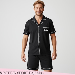 Op de afbeelding: Zwarte katoenen korte pyjamaset met witte bies. Het shirt met korte mouwen heeft een knoopsluiting en een borstzak met de naam "Kevin" geborduurd. De shorts hebben bijpassende witte bies. De tekst "~MENS COTTON SHORT PAJAMA~" staat onderaan.