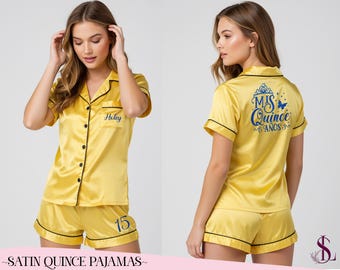 May include: A yellow satin pajama set with black piping, featuring a button-down shirt and shorts. The shirt pocket displays the name Holey, while the shorts feature the number 15. The back of the shirt displays the blue text Mis Quince Años.