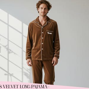 Könnte beinhalten: Ein braunes Samt-Pyjama-Set mit weißen Paspeln, bestehend aus einem Hemd mit Knöpfen und einer passenden Hose. Das Hemd hat eine Brusttasche mit dem Namen "Bob" aufgestickt. Der Pyjama ist einfarbig und wirkt weich.