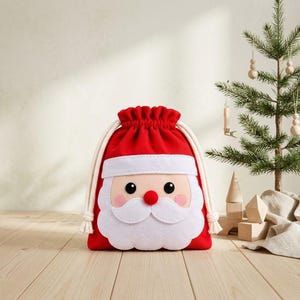 Pode incluir: Um saco de presente vermelho de feltro com cordão, apresentando um design de rosto de Papai Noel. O saco tem uma barba, bigode e aba de chapéu de feltro branco, um nariz vermelho, olhos pretos e bochechas rosadas. Cordas grossas cor de creme.