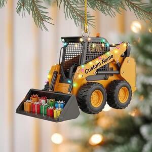 May include: A yellow and black skid steer loader Christmas ornament with the text "Custom Name". The loader's bucket is filled with colorful wrapped gifts, and it is decorated with string lights. The ornament hangs from a gold string.