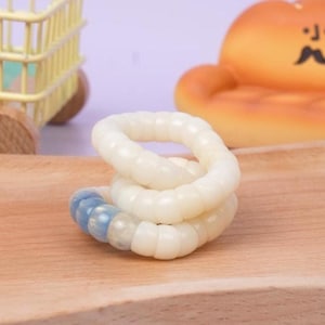 May include: A white and blue fidget toy, composed of interconnected rings, rests on a wooden surface. The toy's design features a series of white, rounded segments that twist and turn, with a section of blue segments. A yellow toy cart is in the background.