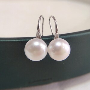 May include: A pair of elegant pearl drop earrings. Each earring features a lustrous, round white pearl suspended from a silver-colored hook. The pearls have a smooth, reflective surface, and the hooks are simple and curved.