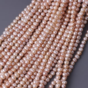May include: Close-up of multiple strands of light peach-colored freshwater pearls. The pearls are oval-shaped and have a lustrous sheen. The strands are arranged closely together, creating a dense, textured surface.
