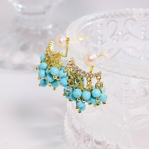 May include: Gold-tone earrings with turquoise beads and a pearl accent. The earrings feature a cluster of small, round turquoise beads hanging from a decorative gold-tone frame. A single pearl is set at the top of each earring.
