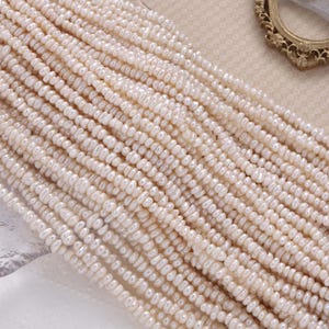 May include: Strands of creamy white freshwater pearls. The pearls are small, irregular in shape, and strung together, creating a textured surface. The pearls are arranged in parallel lines, suggesting they are ready for jewelry making.