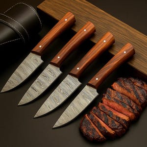 May include: Four steak knives with wooden handles and patterned blades are displayed next to a sliced steak. The knives have a dark wood handle with a single white dot and a patterned blade. A black leather knife case is visible in the background.
